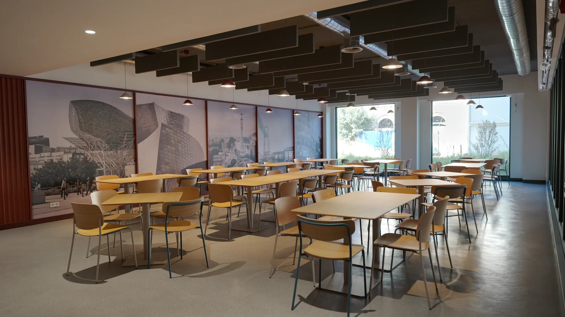 Wooden tables and chairs beside full-height windows and a Barcelona photo mural